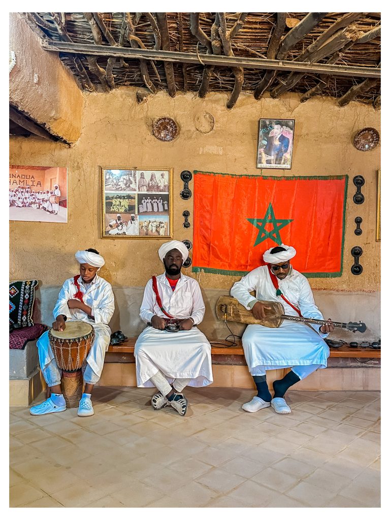 Tres músicos gnawa vestidos de blanco tocando en una casa de Khamlia