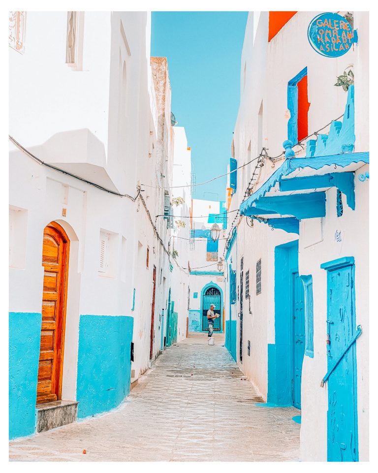 Calle encalada de la medina de Asilah con puertas y paredes azules