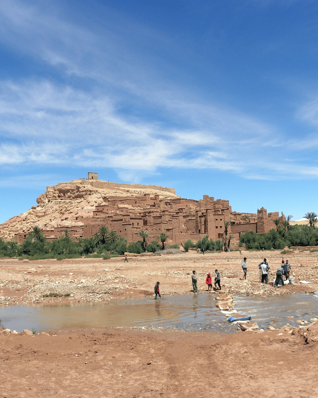 7 Viajeros cruzando el río frente al ksar de Ait Ben Haddou